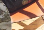 Sac Gerard Darel 24H en toile enduite et cuir avec détails imprimés, posé sur un fauteuil