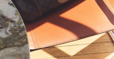 Sac Gerard Darel 24H en toile enduite et cuir avec détails imprimés, posé sur un fauteuil