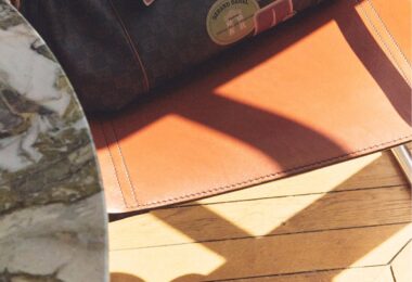 Sac Gerard Darel 24H en toile enduite et cuir avec détails imprimés, posé sur un fauteuil