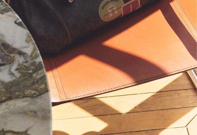 Sac Gerard Darel 24H en toile enduite et cuir avec détails imprimés, posé sur un fauteuil