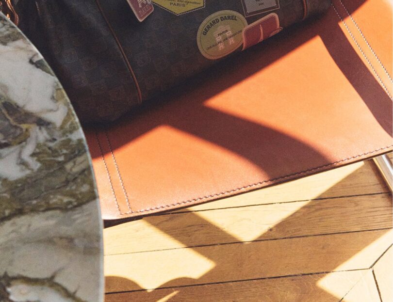 Sac Gerard Darel 24H en toile enduite et cuir avec détails imprimés, posé sur un fauteuil
