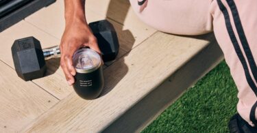Person holding a Spacegoods tumbler beside outdoor training equipment