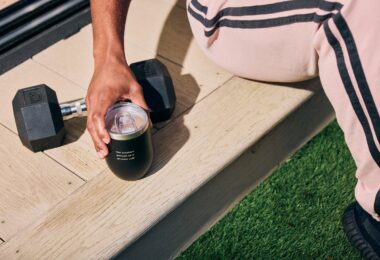 Person holding a Spacegoods tumbler beside outdoor training equipment