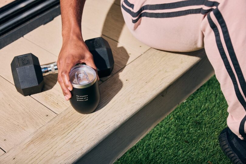 Person holding a Spacegoods tumbler beside outdoor training equipment